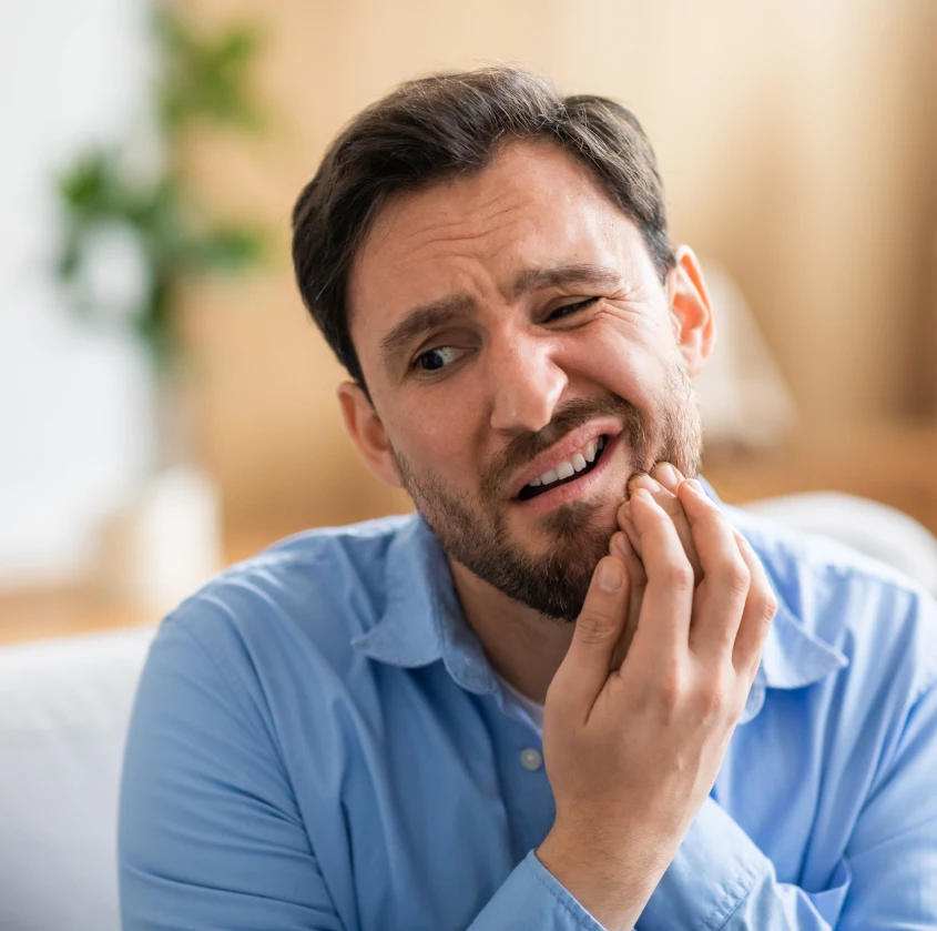 A man wincing in pain while holding his jaw